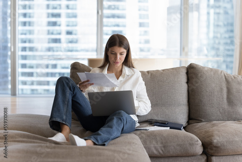 Free Download Busy woman sitting on couch with laptop on laps holding bills, makes easy remote e-payment through e-banking application, student prepare for college exams, studying at home using internet connection - GFXLoad