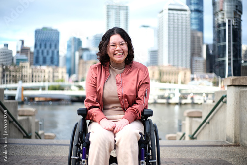 Smiling woman with a disability sitting in a wheel chair with tall buildings behind her photo