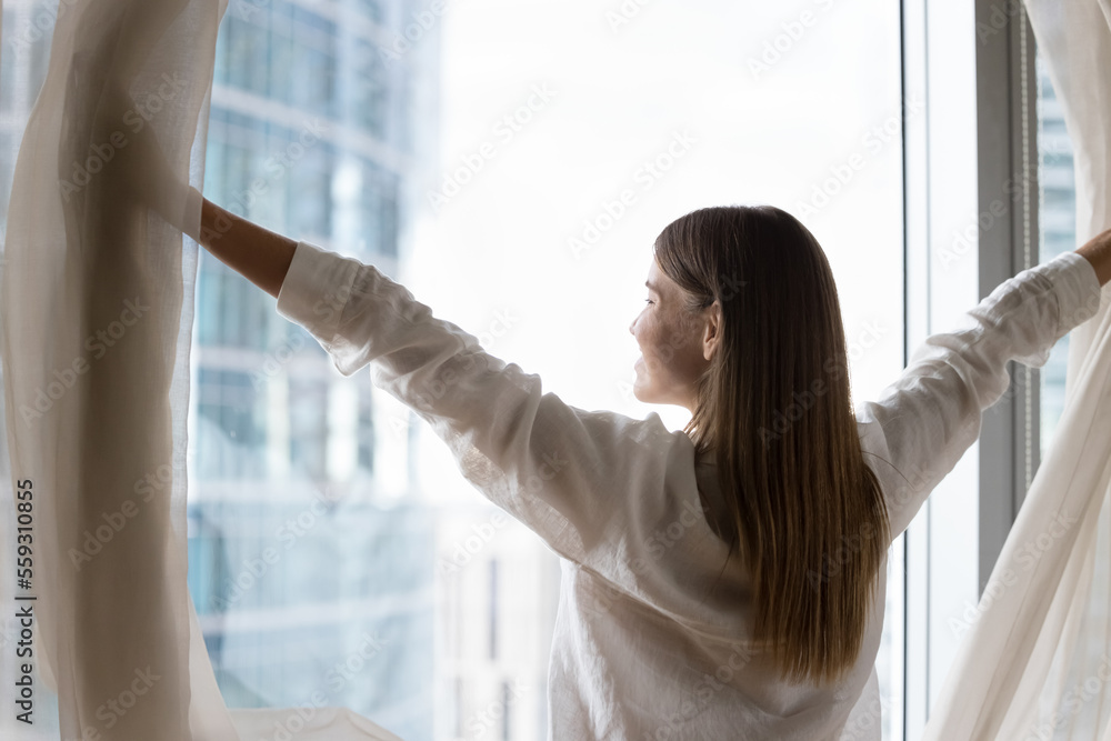 Luxury apartment owner or female traveler opens curtains, welcoming new day, standing near panoramic window, smile admiring big city skyscrapers view, feels happy, enjoy accommodation. Good morning Luxury apartment owner or female traveler opens curtains, welcoming new day, standing near panoramic window, smile admiring big city skyscrapers view, feels happy, enjoy accommodation. Good morning