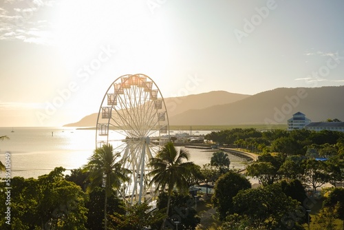 Golden hour over the ferris wheel, treetops, lagoon and hilly backdrop of Cairns Esplanade - Coral Sea, Cairns; Far North Queensland, Australia photo