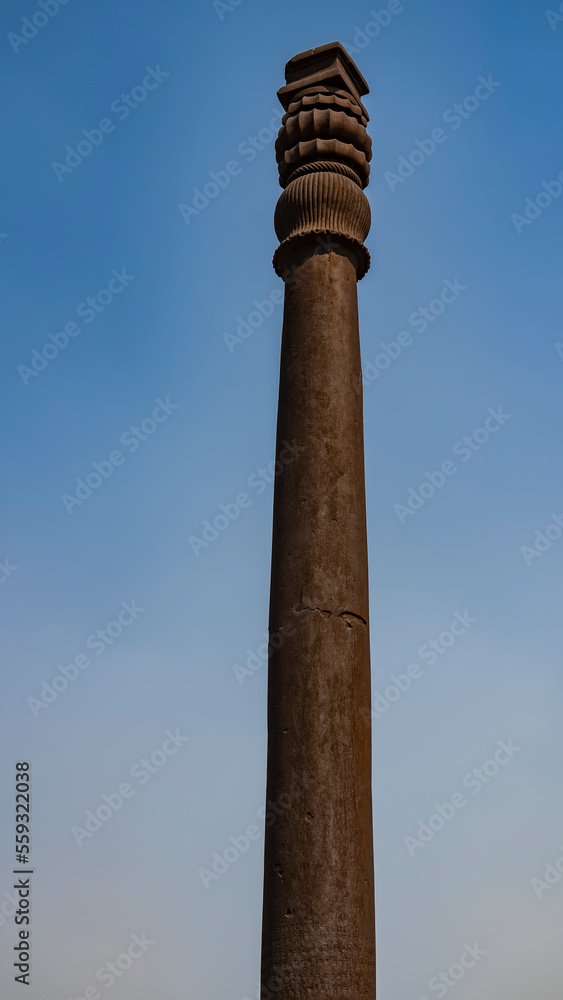 The famous ancient iron pillar, not subject to corrosion, against the blue sky. The top of the column is decorated with cast ornaments. India. Qutub Minar Temple complex. Delhi.