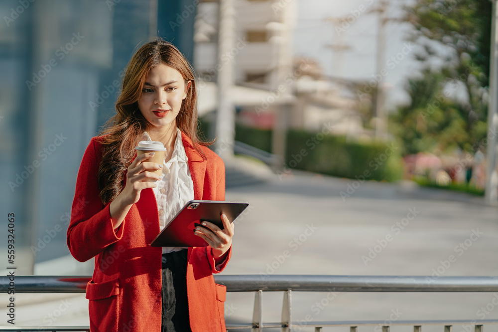 Fototapeta premium Asian women using digital tablet computer and holding coffee to go while working at office.