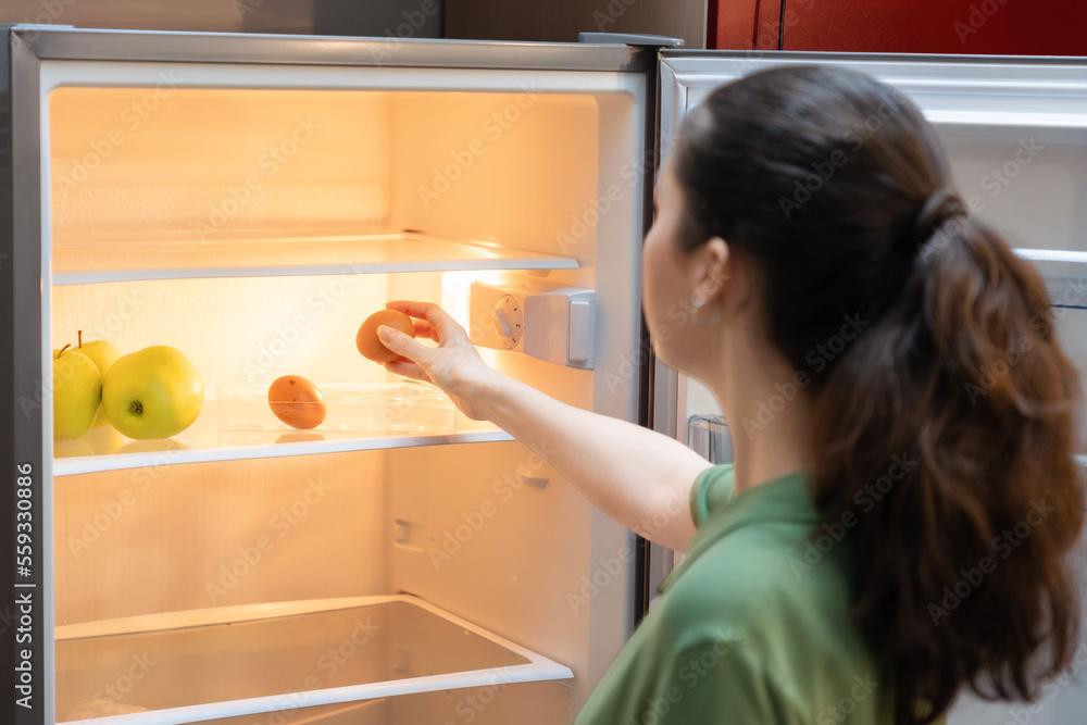 Back view of Caucasian woman takes egg out of empty refrigerator. Concept of nutrition and diet Back view of Caucasian woman takes egg out of empty refrigerator. Concept of nutrition and diet
