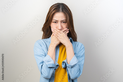 Portrait of pretty brunette hair, disgust smell bad breath strong asian young woman, girl covering, close her mouth with hand, expression face disgusting, dislike odor. Isolated on white background. photo
