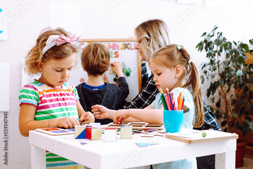Foto Cute little girls with interest fold geometric figures on desk in playroom