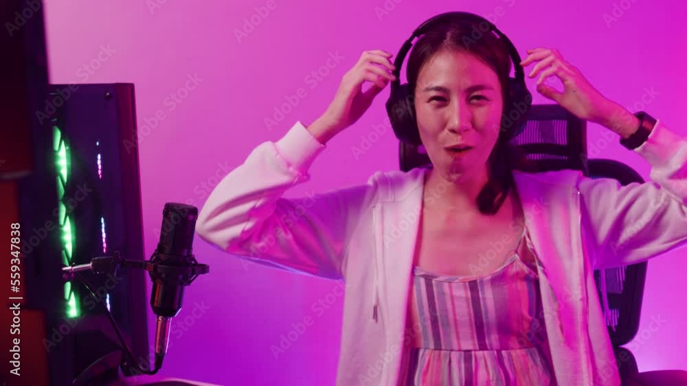 Young Asia female sit on gaming chair wear headset focus concentration computer screen competition at house. Gamer girls raise fist gloats over winning e-sport confidence cross arm looking at camera. Young Asia female sit on gaming chair wear headset focus concentration computer screen competition at house. Gamer girls raise fist gloats over winning e-sport confidence cross arm looking at camera.
