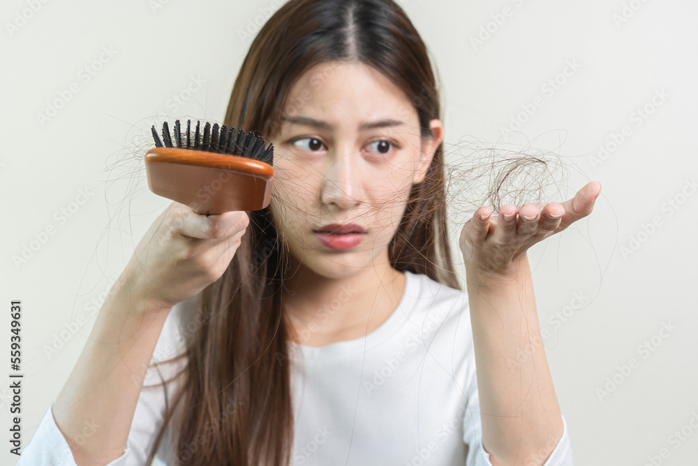 Serious, worried asian young woman, girl holding brush, show her comb, hairbrush with long loss hair problem after brushing, hair fall out on her hand in living room. Health care, beauty treatment. Serious, worried asian young woman, girl holding brush, show her comb, hairbrush with long loss hair problem after brushing, hair fall out on her hand in living room. Health care, beauty treatment.