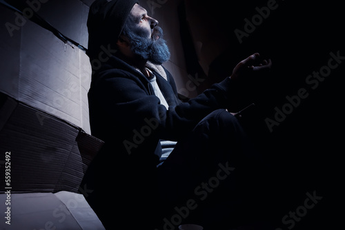 A homeless bearded man sits on boxes on the street and asks for help. Need a homeless person asks for money for food and overnight.