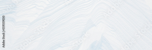Wide panoramic winter background with snowy ground. Natural snow texture. Wind sculpted patterns on snow surface.