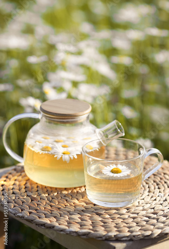 Vertical photo of glass teapot and a cup of herbal camomile tea