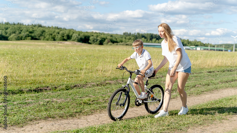 Fototapeta premium loving mother help her cute son ride a bicycle