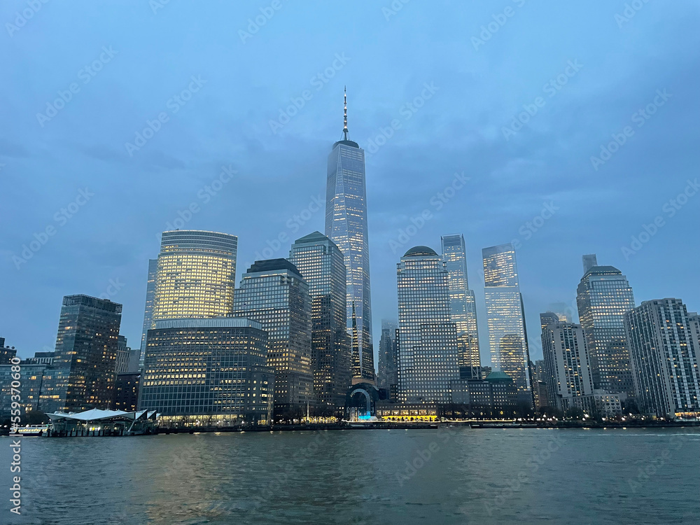 Fototapeta premium Manhattan financial district in downtown from the Hudson river, with the One Word Observatory as New York's tallest skyscraper on a foggy sunset.