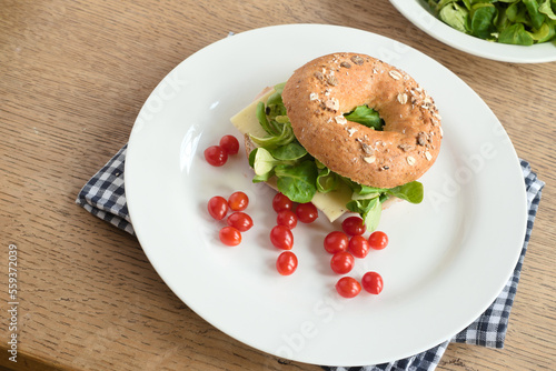 Bagel sandwich with cheese, green lettuce leaves, and cherry tomatoes on a plate