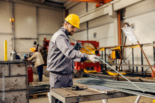 A heavy industry worker is selecting metal bars form a pile and preparing it for a metal processing.