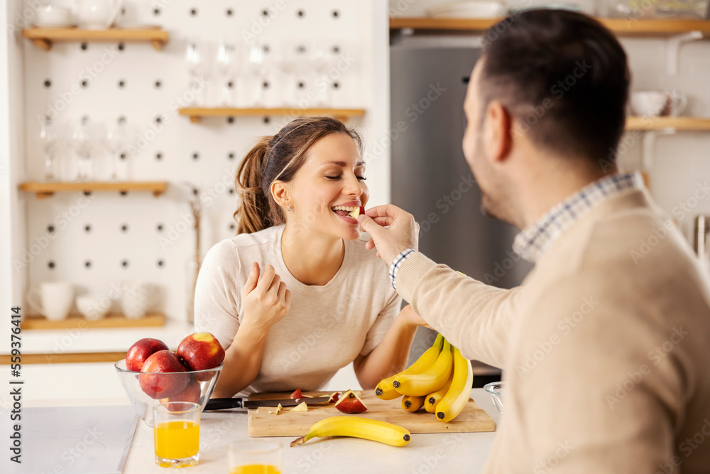 © Dusan Petkovic - A man is feeding his wife with apple at home in kitchen.