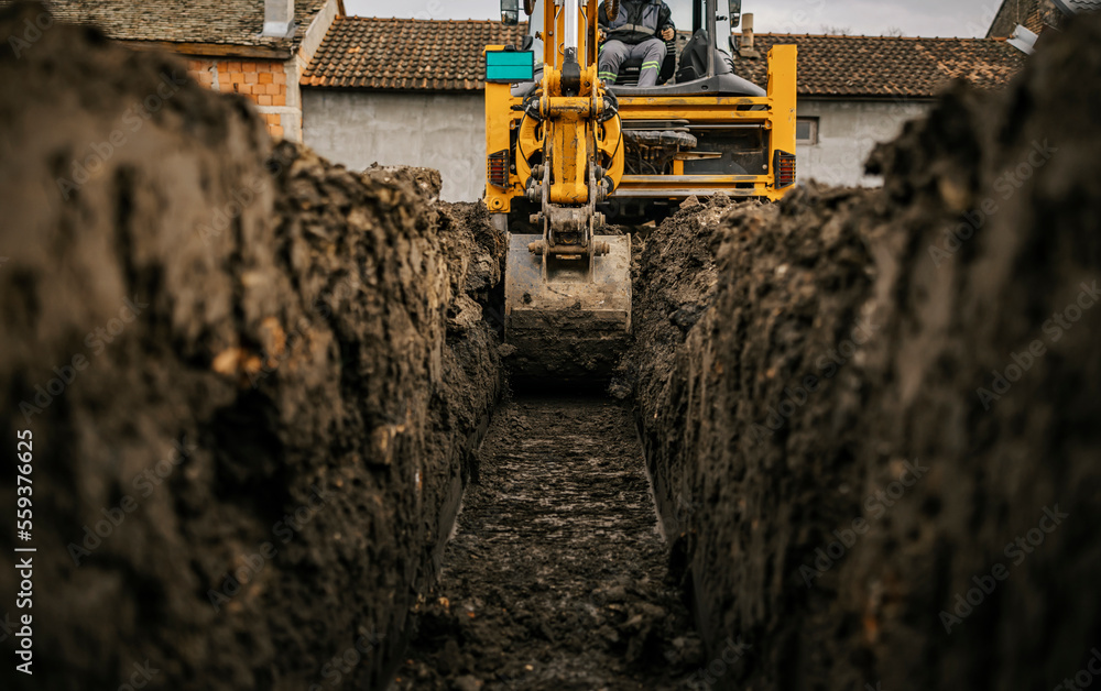 Cropped picture of a backhoe digging soil and making foundation at construction site. - obrazy, fototapety, plakaty 