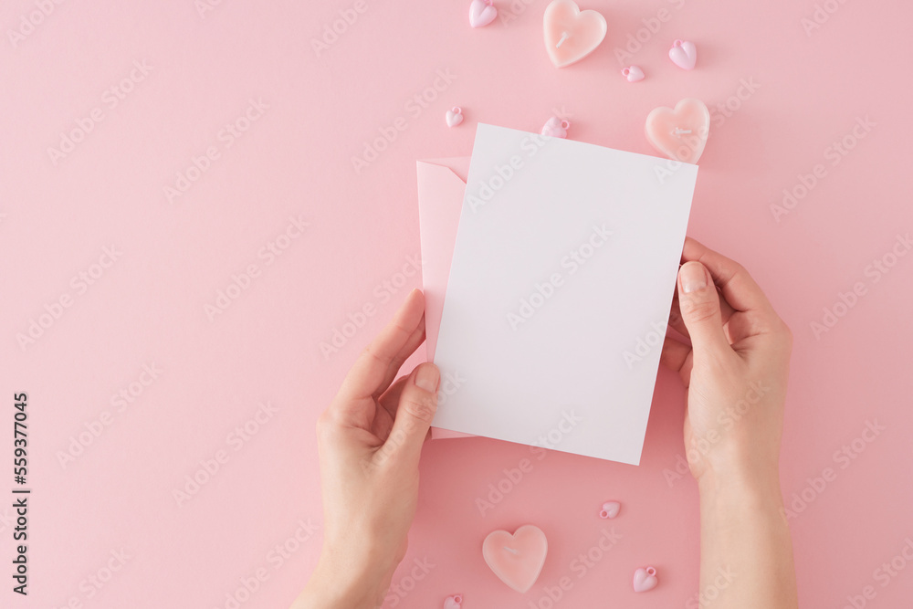 Obraz premium Valentines Day concept. First person top view photo of girl holding envelope with letter over heart shaped candles and baubles on pastel pink background with copy space. Mothers day holiday card idea.