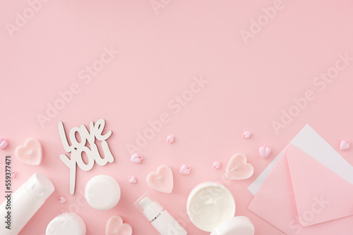 Women day concept. Flat lay photo of cosmetic bottles, cream jars, heart shaped candles, envelope and inscription love you on pastel pink background with copy space. Mother's day Or Valentines idea.