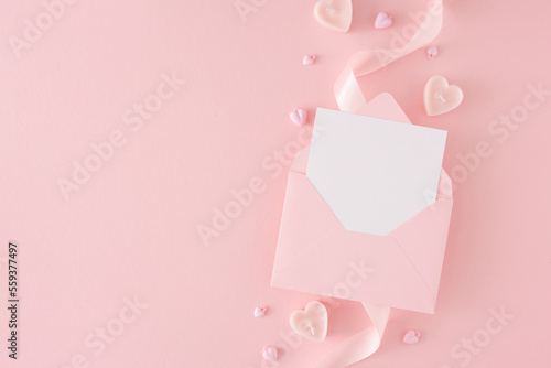 Women day concept. Flat lay photo of envelope with letter, silk ribbon and heart shaped candles on pastel pink background with copy space. Mother's day Or Valentines idea. © Goncharuk film