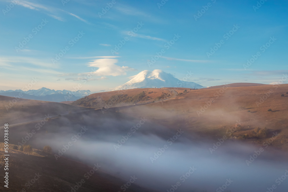 Soft focus. Elbrus  Mountain in a dense morning fog and sunny slope. Mystical landscape with beautiful snowy rocks in low clouds. Beautiful mountain foggy scenery.