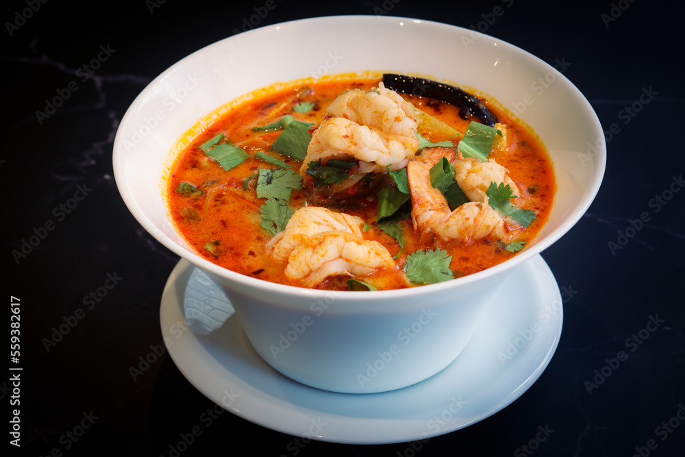 A bowl of traditional famous Thai spicy soup with shrimp (Tom Yum Kung in Thai) with isolated black background.  It's a type of Thai hot and sour soup where the iconic flavors come from 3 herbs