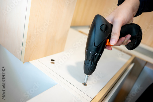 Wallpaper Mural Home renovation or House remodeling concept. Male hand furniture assembler or Interior construction worker using electric drill screwdriver installing wooden counter and cabinet of new kitchen. Torontodigital.ca