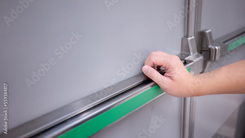 Male hand pushing stainless steel panic bar opening the emergency fire exit door in public building. Fire escape concept photo