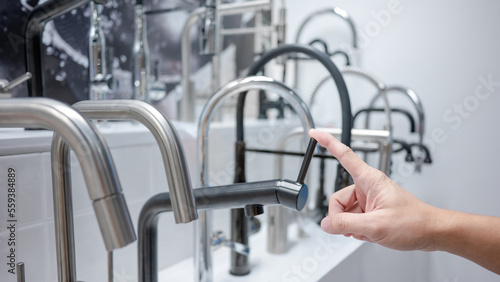Slika na platnu Male hand choosing modern black water tap in furniture store