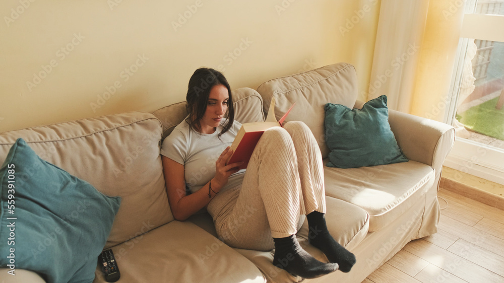 Young woman reading book sitting on the sofa at home