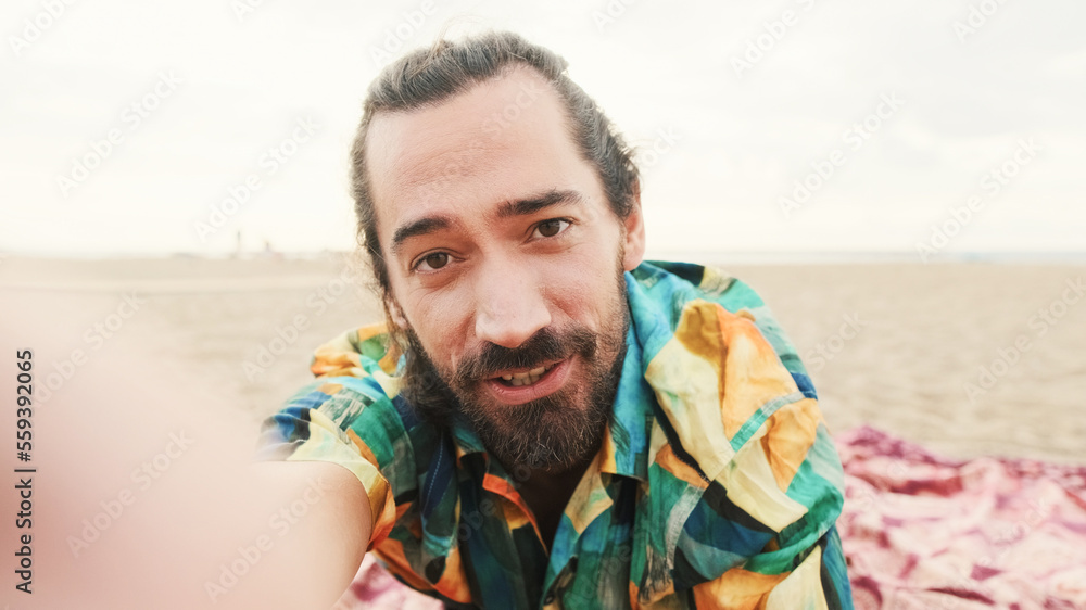 Young happy man lies talking by video call on the beach