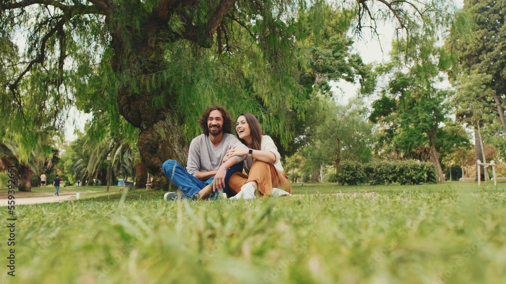 Happy smiling couple talking while sitting on blanket in park Happy smiling couple talking while sitting on blanket in park
