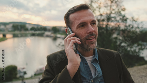 Close up, man talking on mobile phone while standing on the embankment of the river