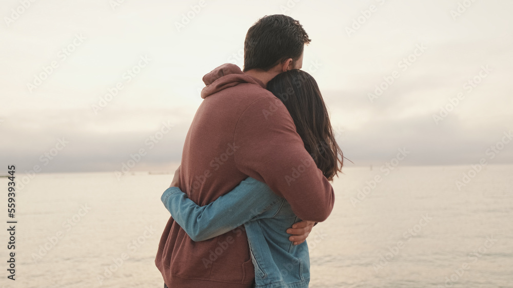 Young couple standing embracing on seascape background. Back view