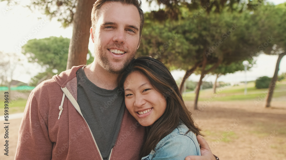 Close up, laughing couple hugging each other while standing in the park. looking at camera