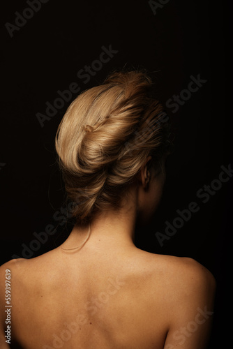Natural beauty concept. Woman portrait with naked shoulders and hair bun. Model standing back to camera in black studio background with copy space. Toned image with yellow color. Vintage style
