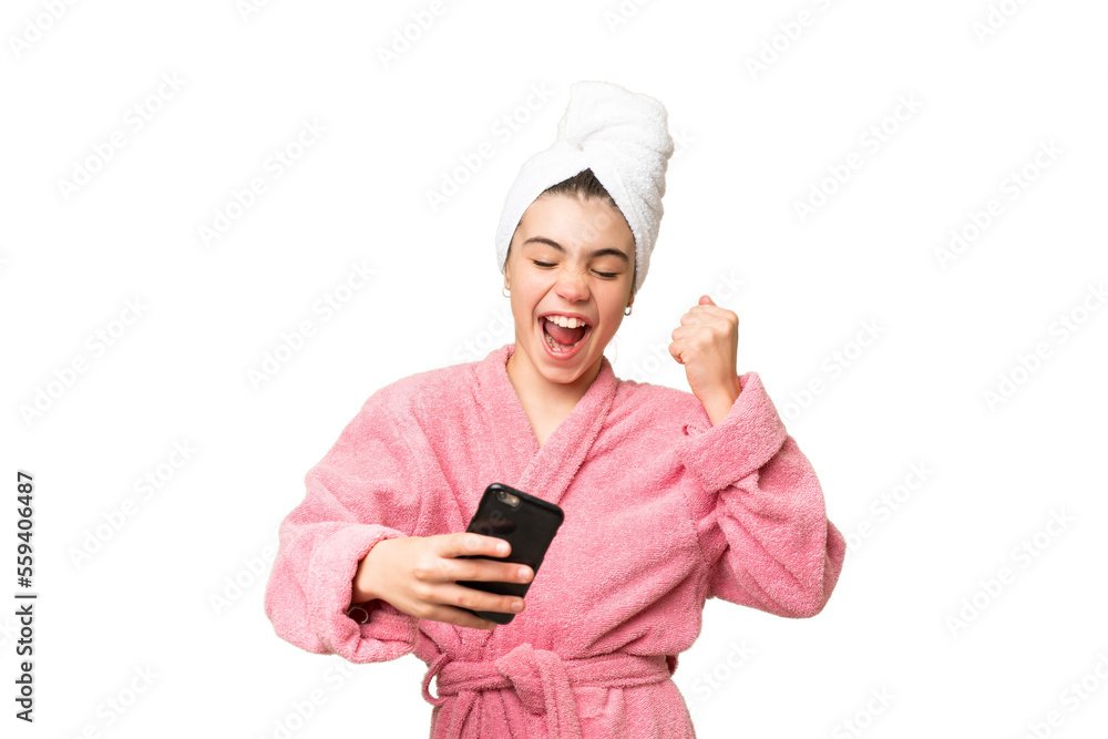 Little girl in a bathrobe over isolated chroma key background with phone in victory position Little girl in a bathrobe over isolated chroma key background with phone in victory position