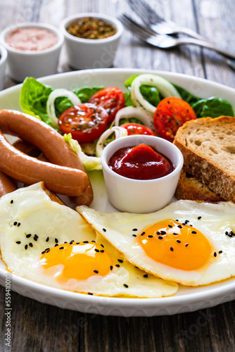 Breakfast - sunny side up egg, boiled sausages and vegetables served on wooden table 