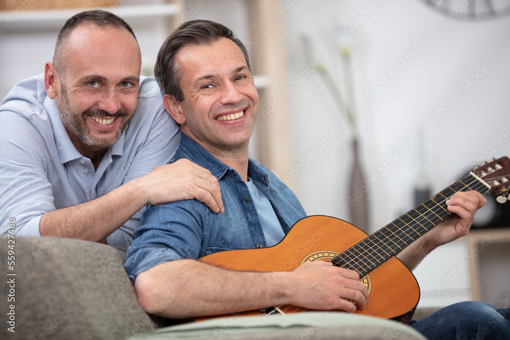 Fototapeta premium young gay couple sitting on sofa and playing guitar