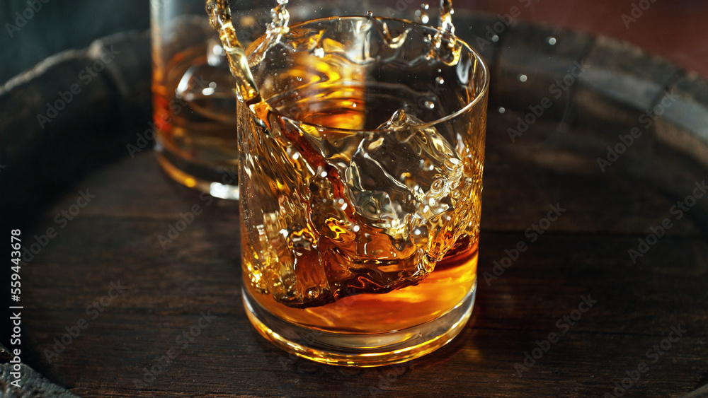 Falling ice cube into whiskey glass, macro shot.