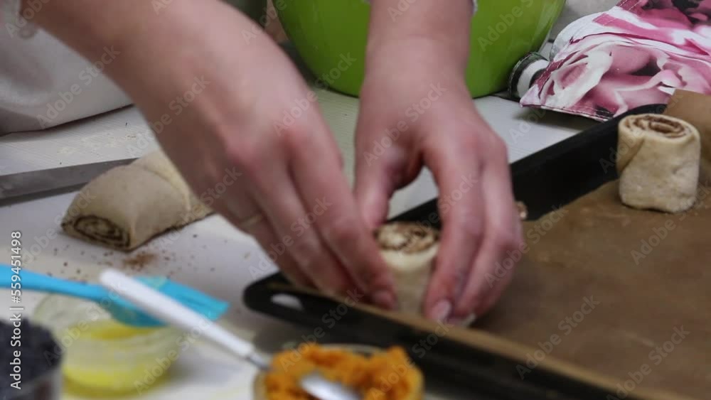The woman lays chopped dough with cinnamon on a baking sheet. Makes cinnamon buns. Ingredients on the table.