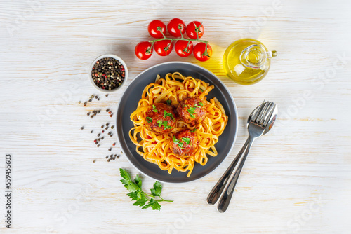 Homemade spaghetti with tomato sauce meatballs and spices served in black plate on white wooden background. Tasty cooked pasta with minced beef meat balls and food ingredients. Top View, Flat lay.