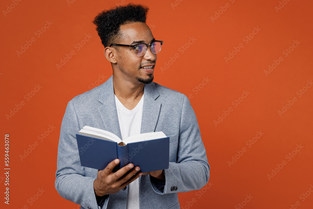Young smart confident employee business man corporate lawyer wearing classic formal grey suit shirt glasses work in office read book look aside on area isolated on plain red orange background studio.