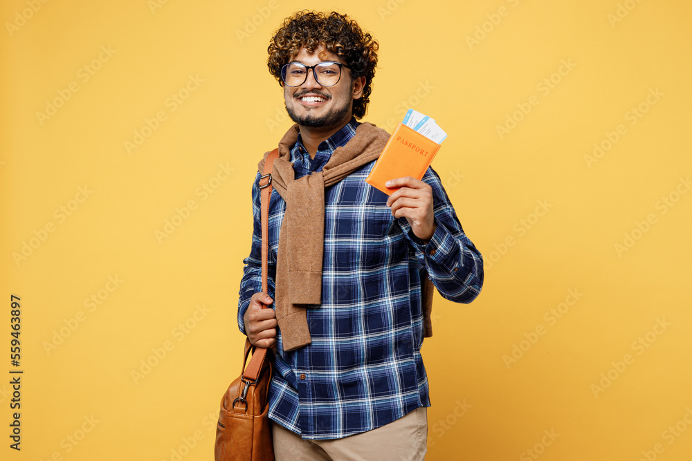 Side view traveler Indian boy IT student wears casual clothes hold passport ticket isolated on yellow background. Tourist travel abroad in free time rest getaway. Air flight trip university concept. Side view traveler Indian boy IT student wears casual clothes hold passport ticket isolated on yellow background. Tourist travel abroad in free time rest getaway. Air flight trip university concept.