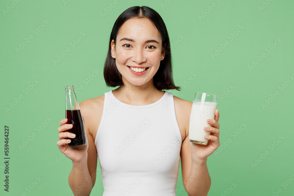 Young woman wear white clothes hold in hands bottle of soda pop fizzy cola water glass of milk isolated on plain pastel green background. Proper nutrition healthy fast food unhealthy choice concept. Young woman wear white clothes hold in hands bottle of soda pop fizzy cola water glass of milk isolated on plain pastel green background. Proper nutrition healthy fast food unhealthy choice concept.