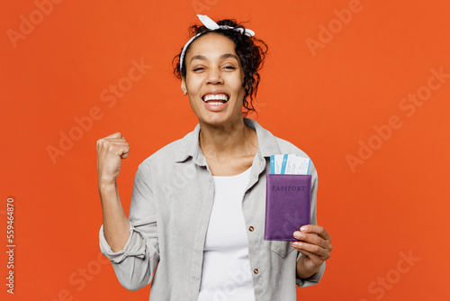 Traveler young woman wear grey shirt hold passport ticket do winner gesture isolated on plain orange background. Tourist travel abroad in free spare time rest getaway. Air flight trip journey concept. #559464870