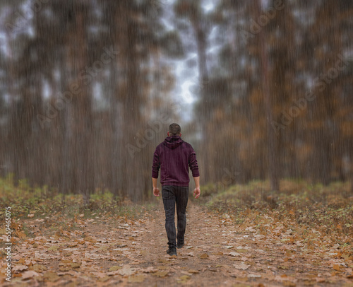 A lonely, sad man in the autumn forest walks along a path in the rain. Autumn depression, feelings, emotions. Meditation. In the center of nature. Copy space