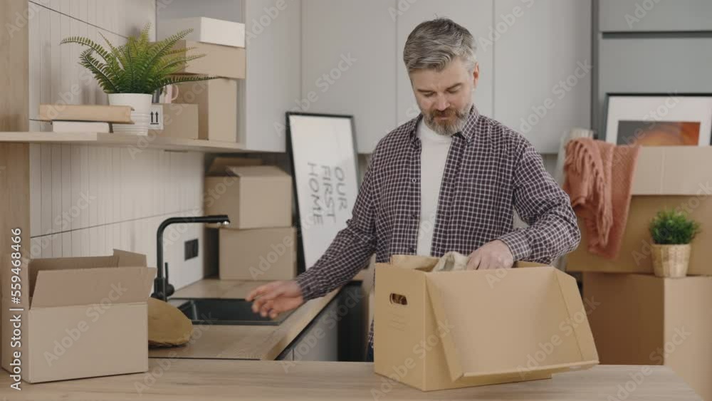 Male owner unpack things from the box at moving new home. Attractive man unpacking interior objects from cardboard boxes relocating to new apartment. New home and relocation concept. Male owner unpack things from the box at moving new home. Attractive man unpacking interior objects from cardboard boxes relocating to new apartment. New home and relocation concept.