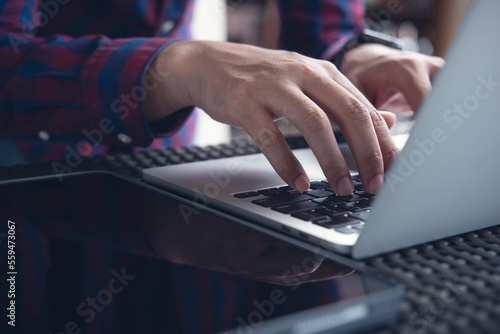 Man sitting at table working on laptop computer, hand typing keyboard. Casual business man, freelancer online working at coffee shop, surfing the internet © tippapatt