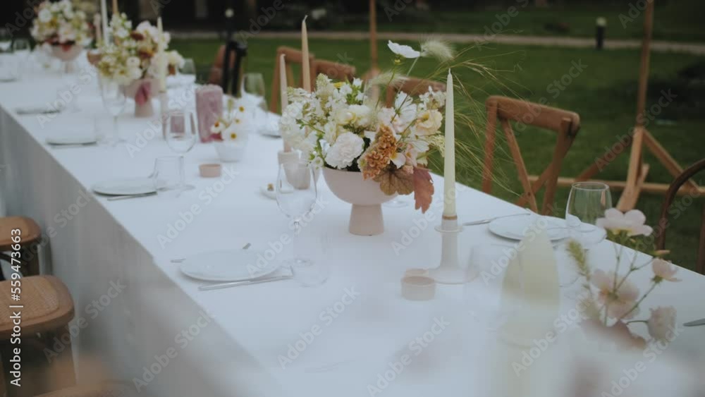 Close-up wedding table setting with pastel wild flowers, candles, old fashioned chairs and retro lamps on the background at small wedding party, slow motion. Close-up wedding table setting with pastel wild flowers, candles, old fashioned chairs and retro lamps on the background at small wedding party, slow motion.