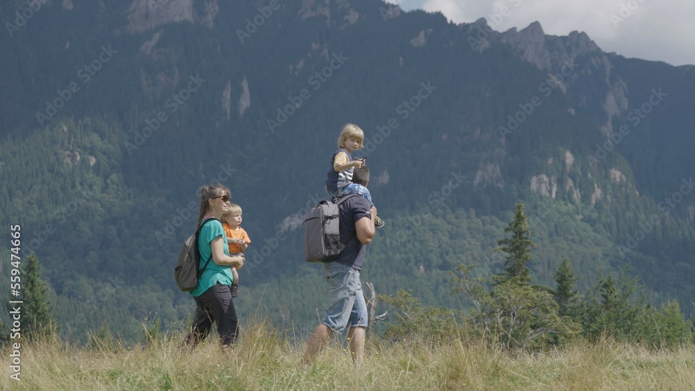Mother hold baby, father give a piggy ride to his son, family hike on mountain